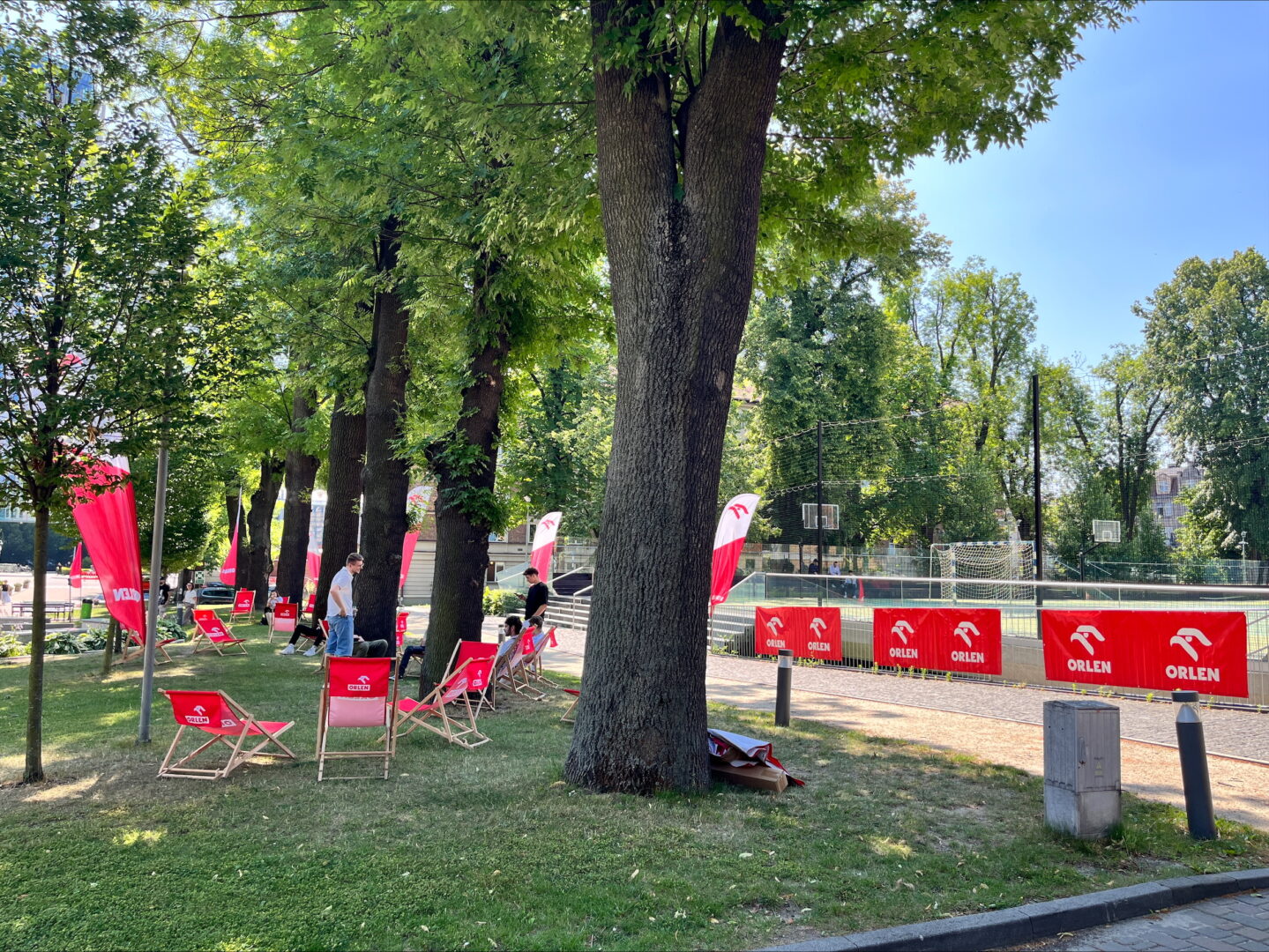 Kampus UEK, na tle drzewa, boisko i plakaty Orlen